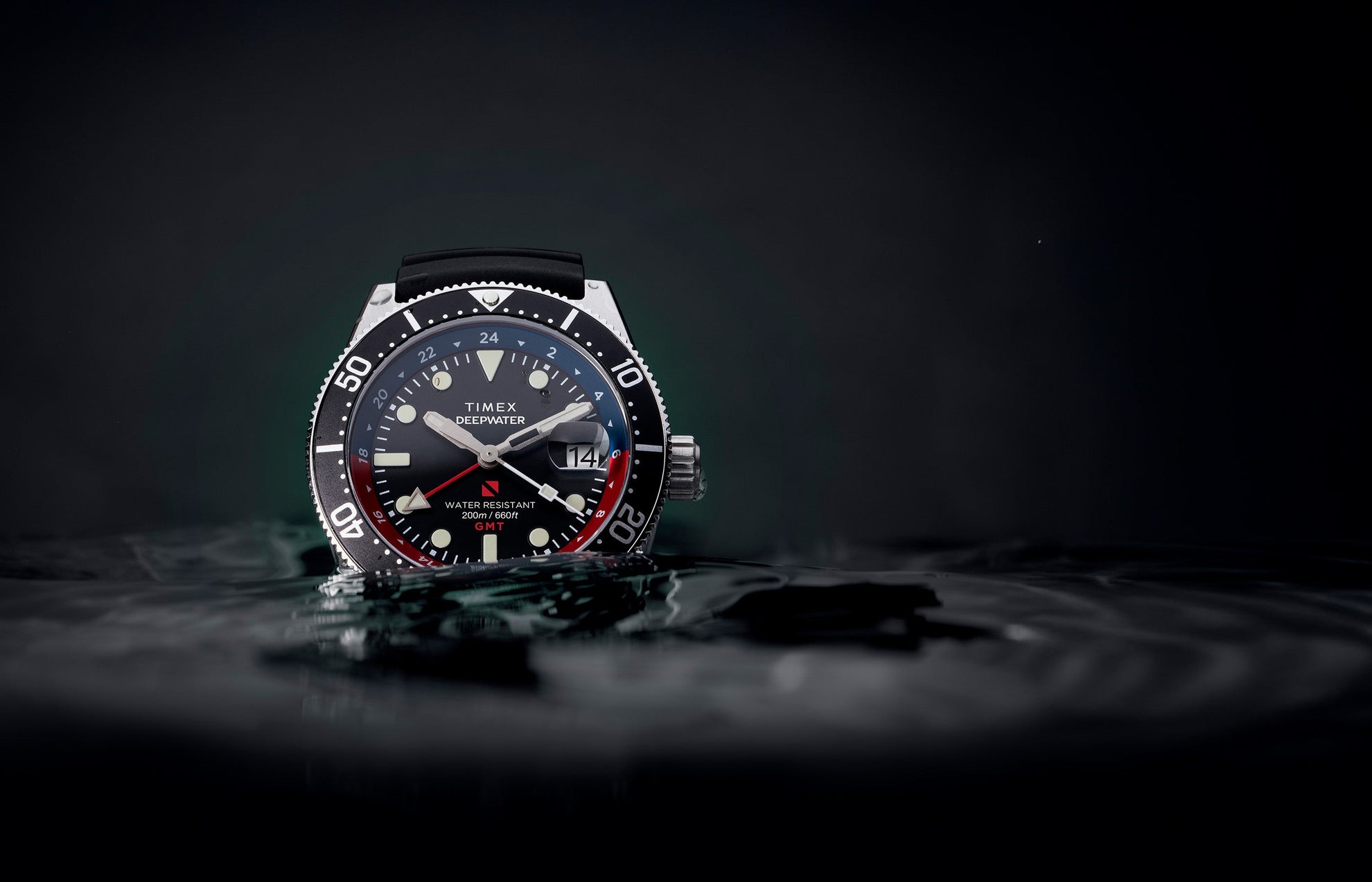 Timex Deepwater Reef 200 GMT dive watch with black dial, black strap, and red-blue bezel partially submerged in water, emphasizing its rugged design and 200-meter water resistance.