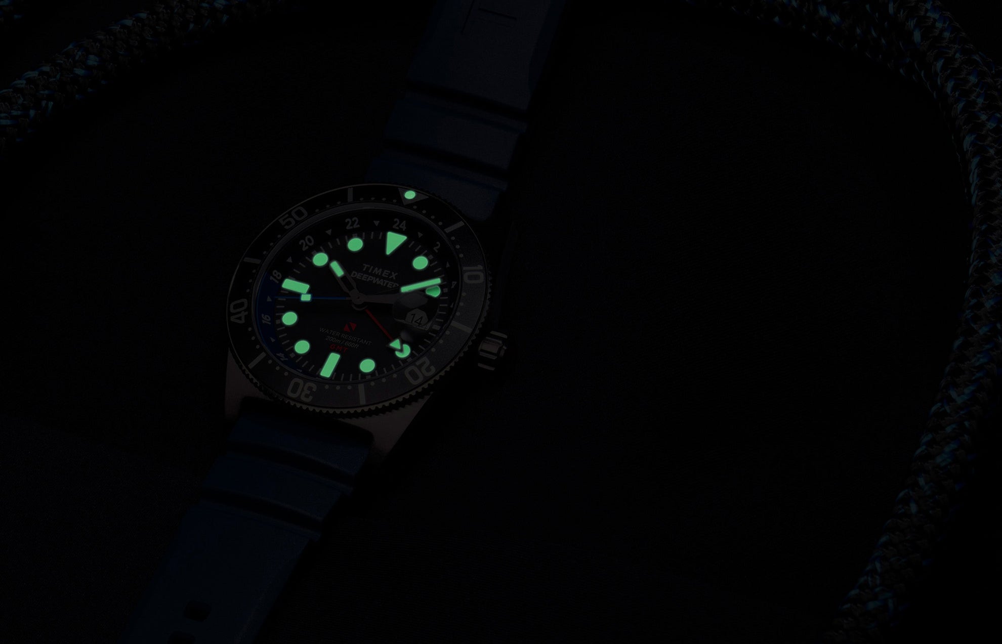 Timex Deepwater Reef 200 GMT glowing in the dark, showing bright green luminescent hour markers and hands for optimal underwater visibility.