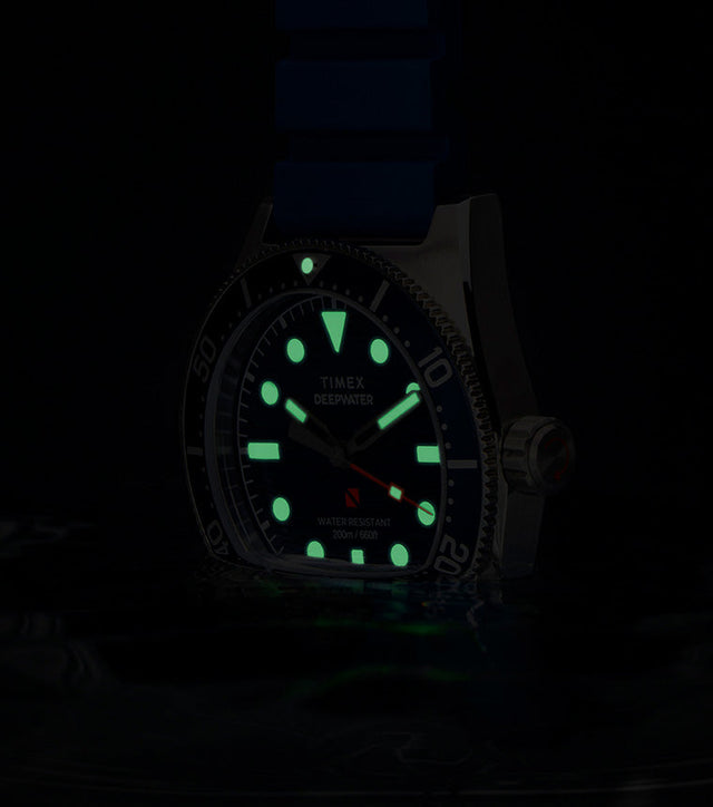 Timex Deepwater Reef 200 watch glowing underwater, with luminous markers and hands shining green in low light, emphasizing dive-ready legibility.