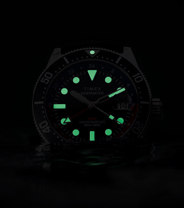 Timex Deepwater Reef 200 GMT glowing in darkness, showing bright green luminescent markers and hands for underwater visibility.
