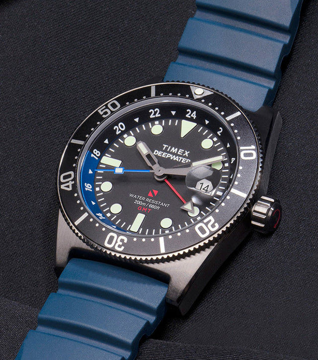 Timex Deepwater Reef 200 GMT dive watch with blue strap and black dial featuring a blue and black bezel, photographed against dark neoprene fabric and matching rope detailing.