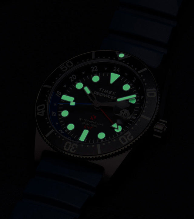 Timex Deepwater Reef 200 GMT glowing in the dark, showing bright green luminescent hour markers and hands for optimal underwater visibility.