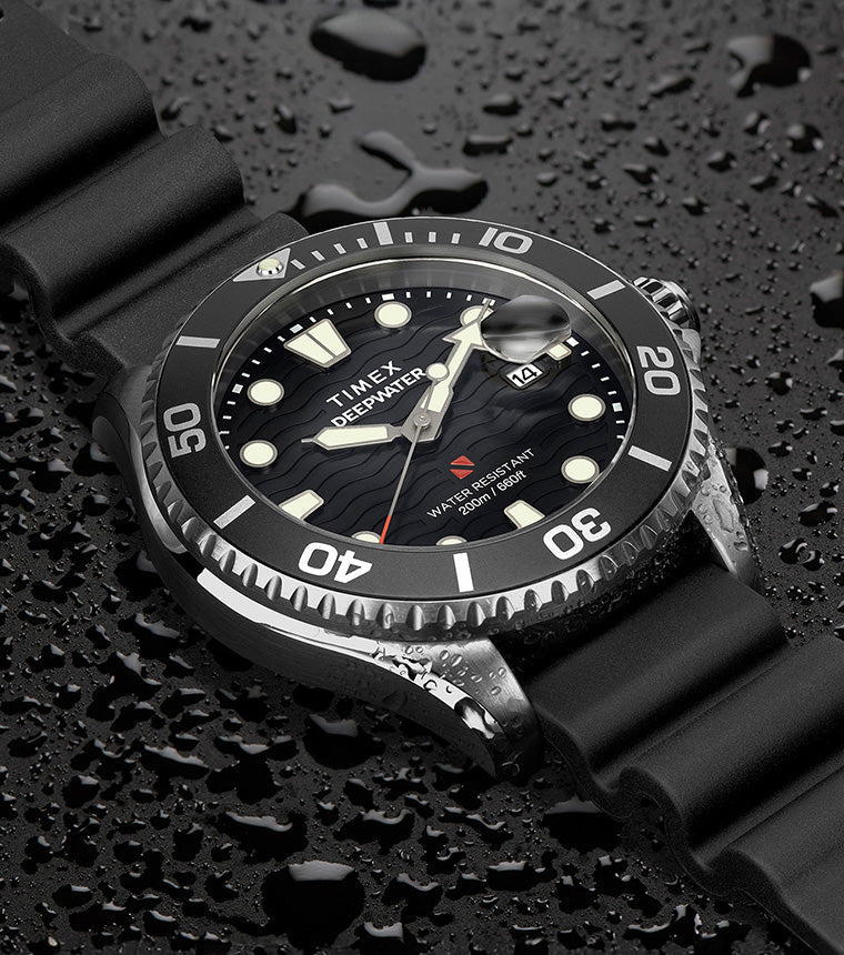 Timex Deepwater Meridian 200 dive watch with black strap and wave-textured black dial resting on a surface covered in water droplets, emphasizing its 200-meter water resistance and rugged construction.