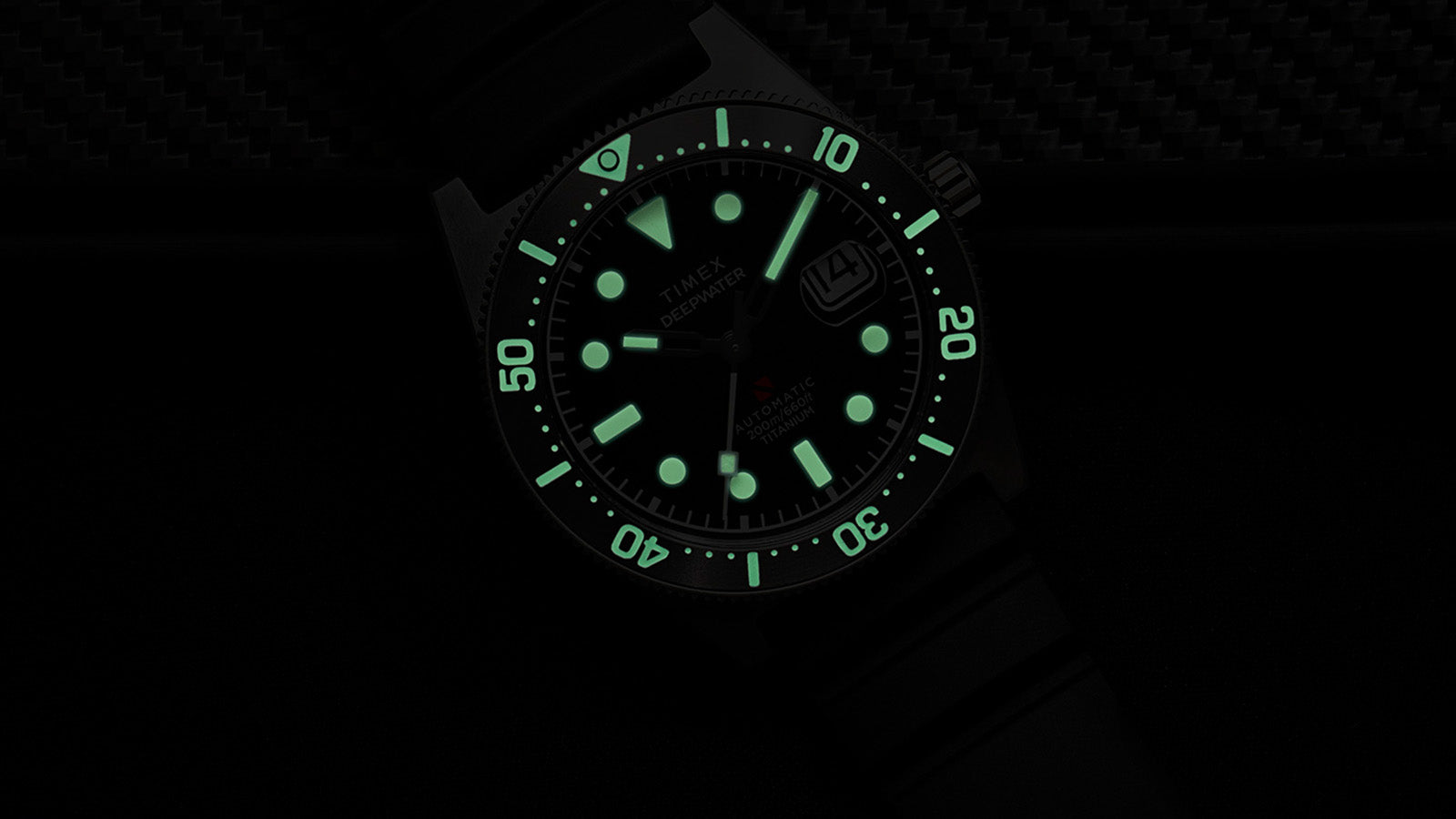 Timex Deepwater Reef 200 Titanium Automatic watch glowing in darkness, showing strong lume on hands, hour markers, and bezel numerals.