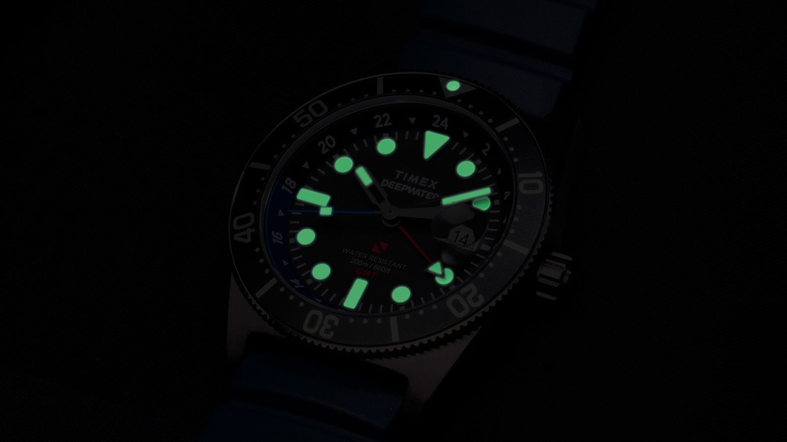 Timex Deepwater Reef 200 GMT glowing in the dark, showing bright green luminescent hour markers and hands for optimal underwater visibility.