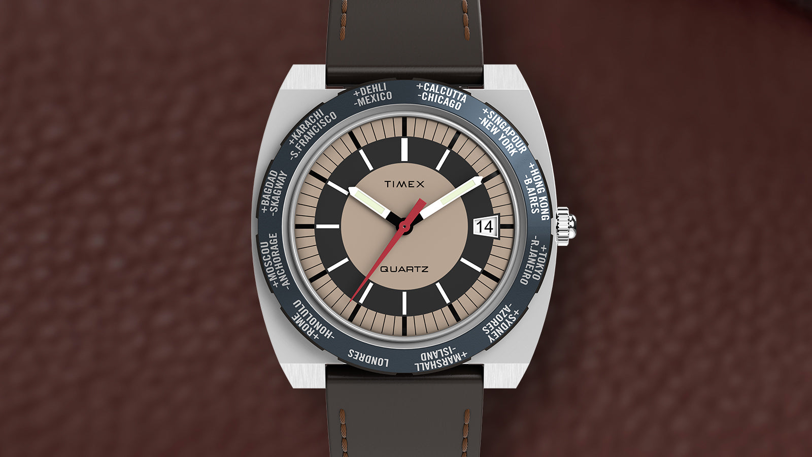 Top-down view of the Q Timex® 1972 World Time watch with tan and black dial, world time bezel featuring major cities, and brown leather strap laid on textured brown leather.