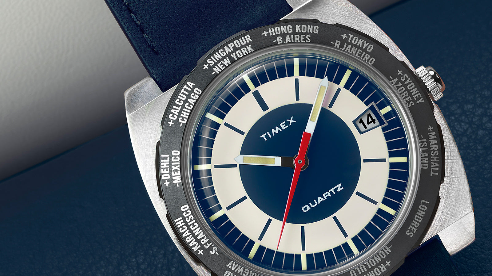 Front view of the Q Timex® 1972 World Time showing the dual-tone blue and cream dial, brushed case, and rotating world time bezel engraved with major cities.