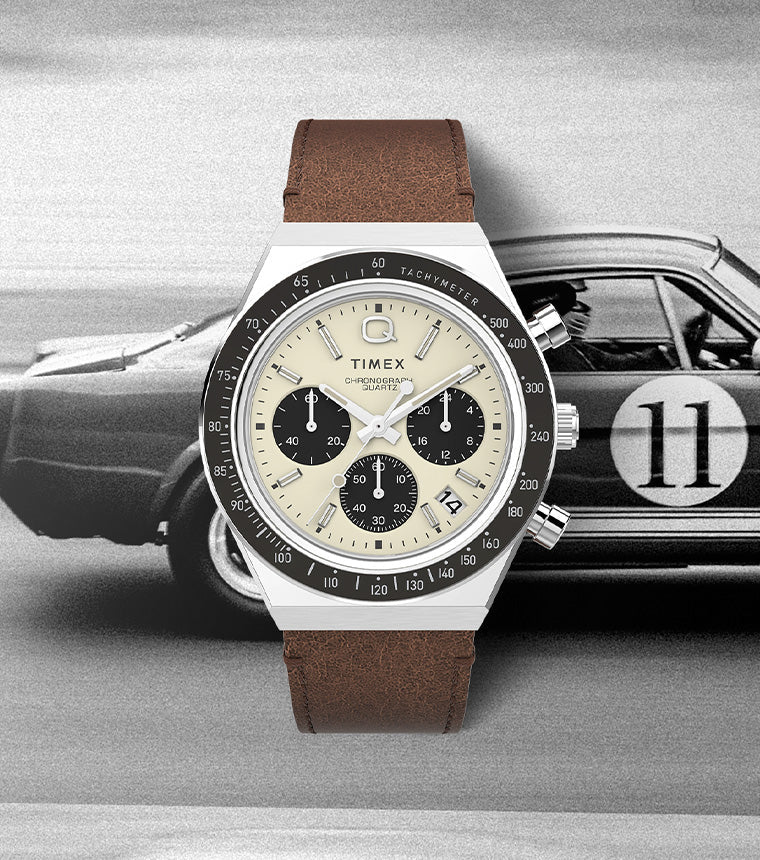 Q Timex Chronograph watch with a cream dial, black sub-dials, and brown leather strap displayed over a vintage racing car background, evoking a classic motorsport aesthetic.
