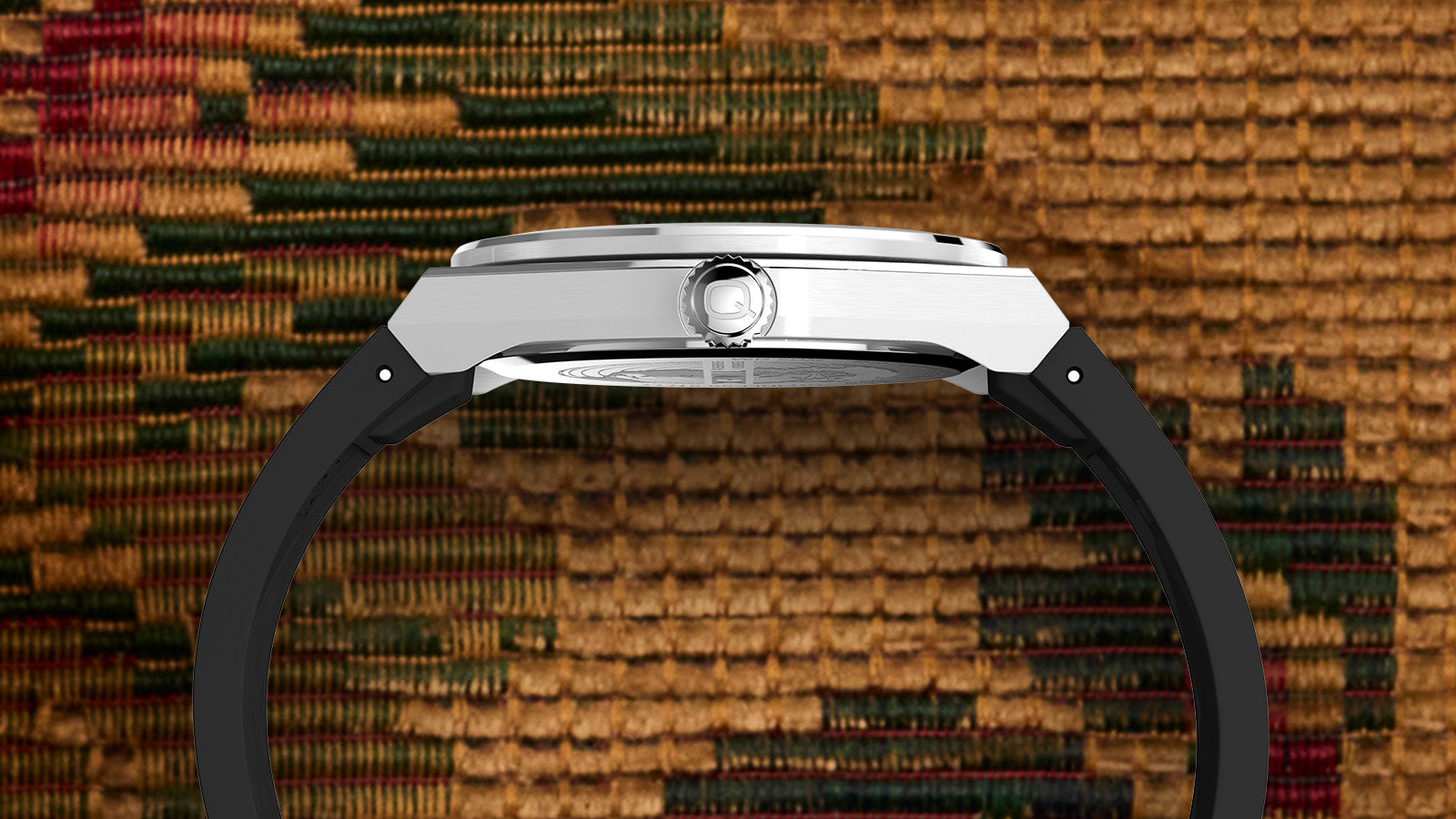 Profile view of the Q Timex® Continental GMT showing its brushed stainless-steel case, slim profile, and engraved “Q” logo crown with black strap attachment.