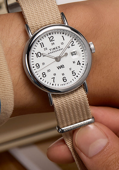 Timex Weekender watch with beige strap worn on a wrist, styled casually with a denim jacket sleeve.