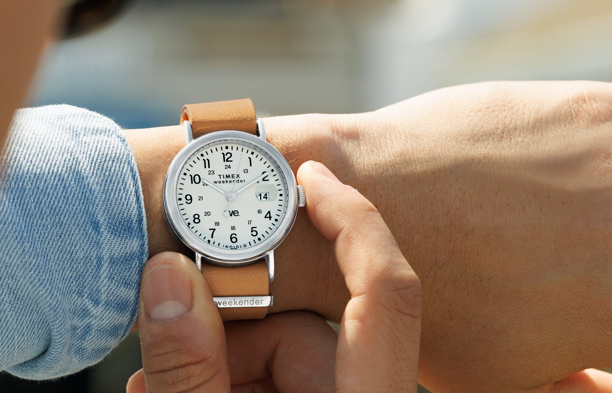 Person adjusting the crown of a Timex Weekender watch with white dial and tan leather strap, close-up wrist shot.