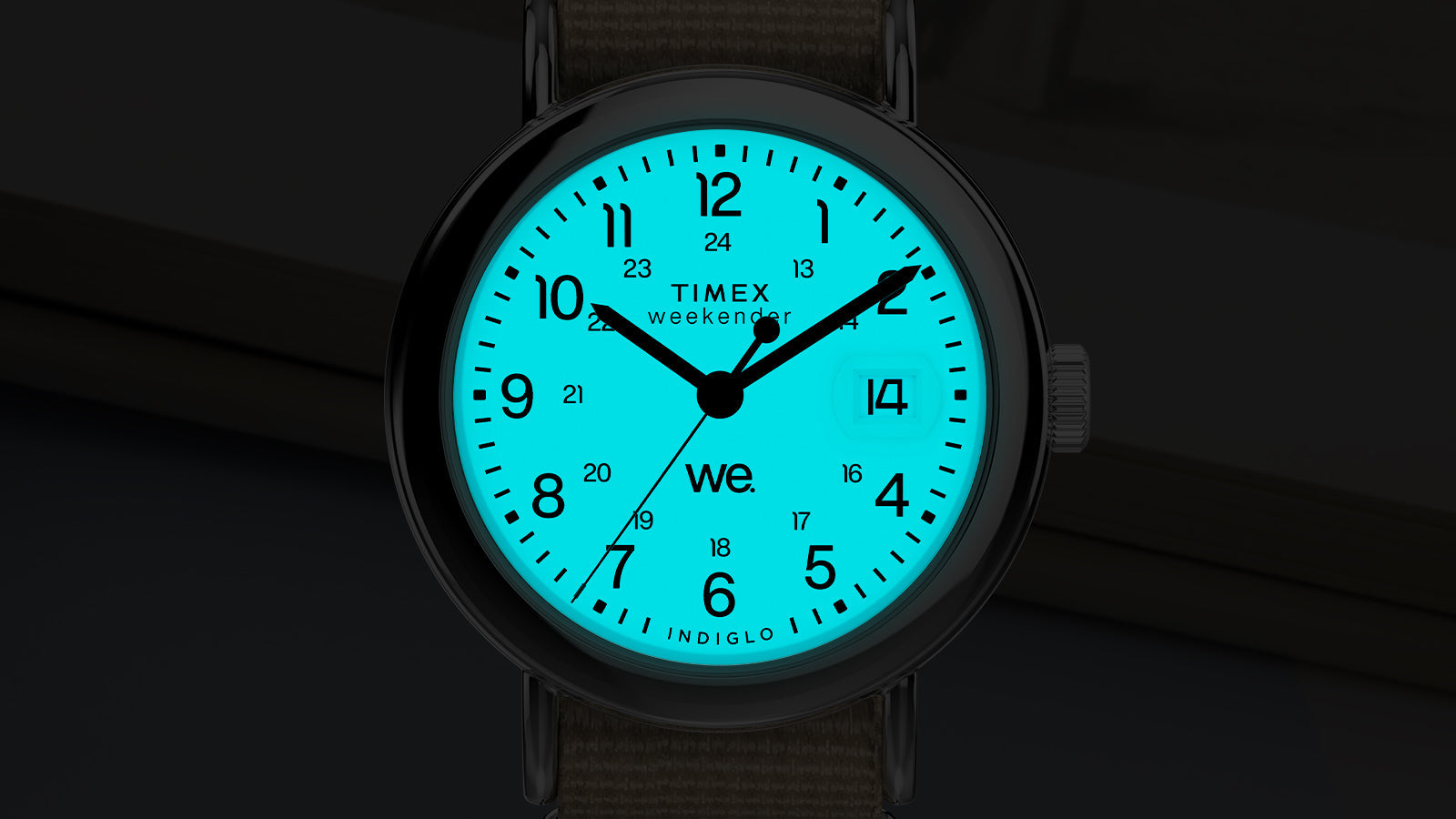 Timex Weekender dial illuminated with Indiglo backlight, glowing blue in the dark and showing clear numerals and date.