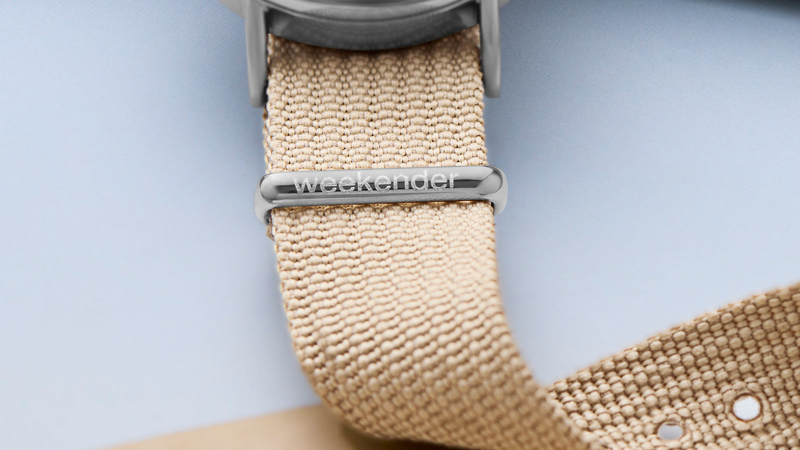 Close-up of beige fabric strap with “weekender” engraved on the polished silver-tone loop.