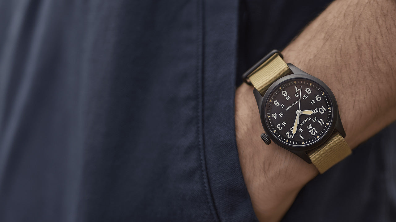 The Timex Expedition Field Post Solar watch with black dial and khaki strap worn on the wrist, paired with a navy jacket for an outdoor-inspired look.