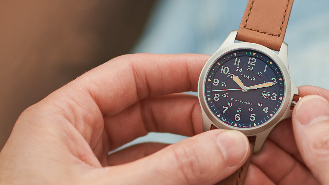 Timex Expedition Field Post Solar watch with a navy dial and silver-tone case shown in hand, with the crown being adjusted.