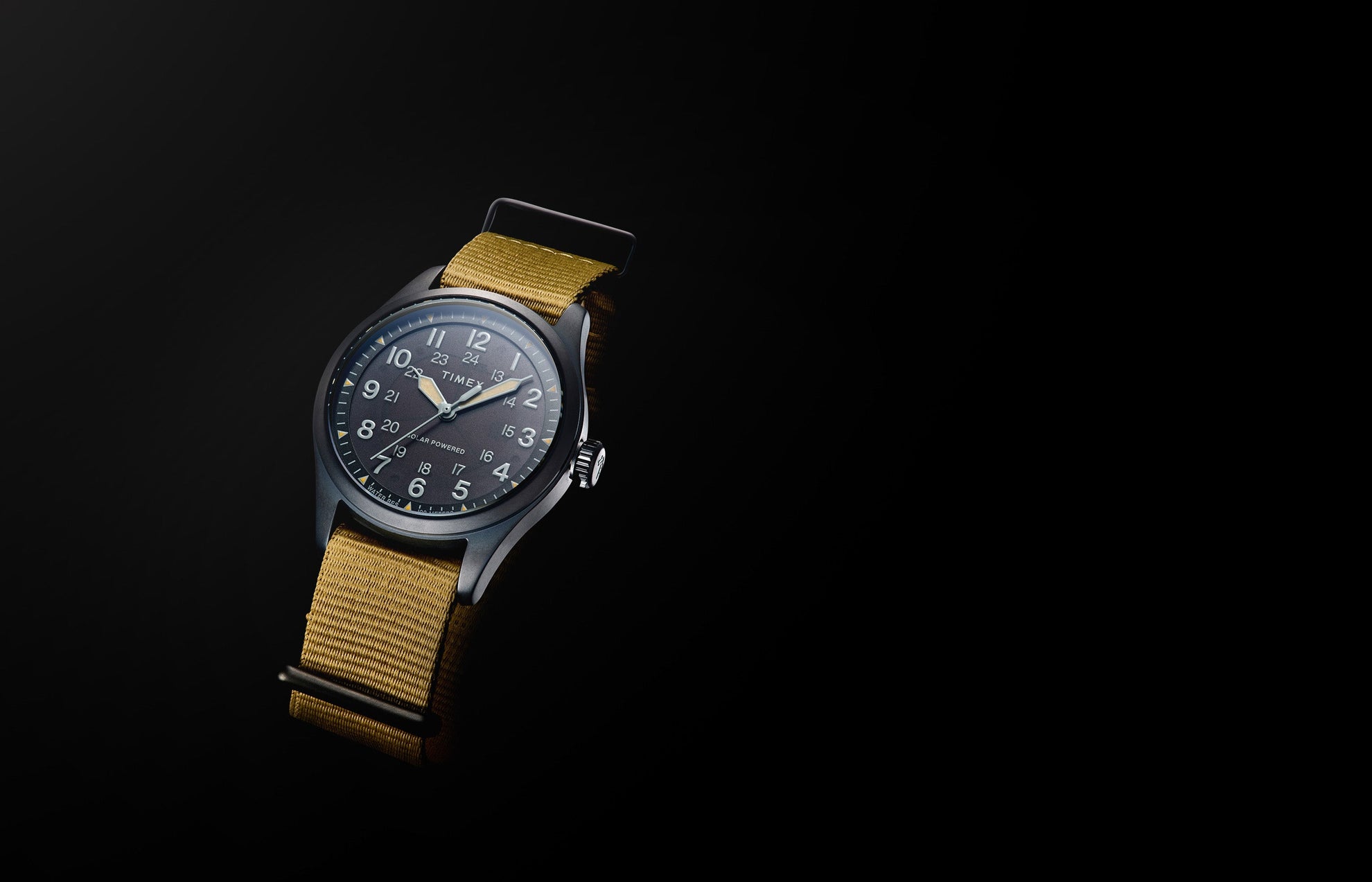 A Timex Expedition Field Post Solar watch with a black dial, luminous hands, white Arabic numerals, and khaki fabric strap shown against a black background.