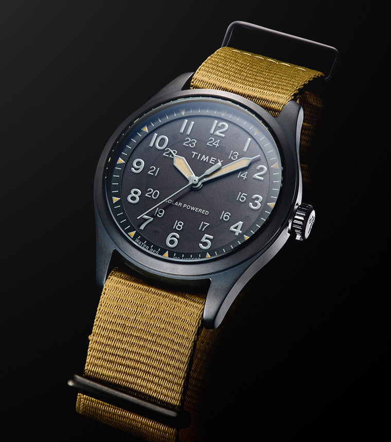A Timex Expedition Field Post Solar watch with a black dial, luminous hands, white Arabic numerals, and khaki fabric strap shown against a black background.