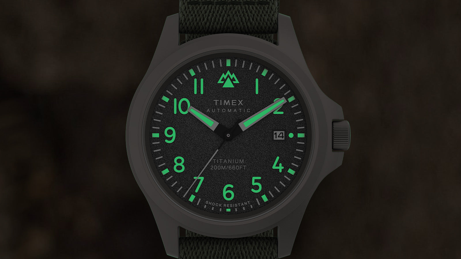 Timex Expedition North Titanium Automatic watch face glowing in the dark with luminous green hands, numerals, and markers against the black dial.