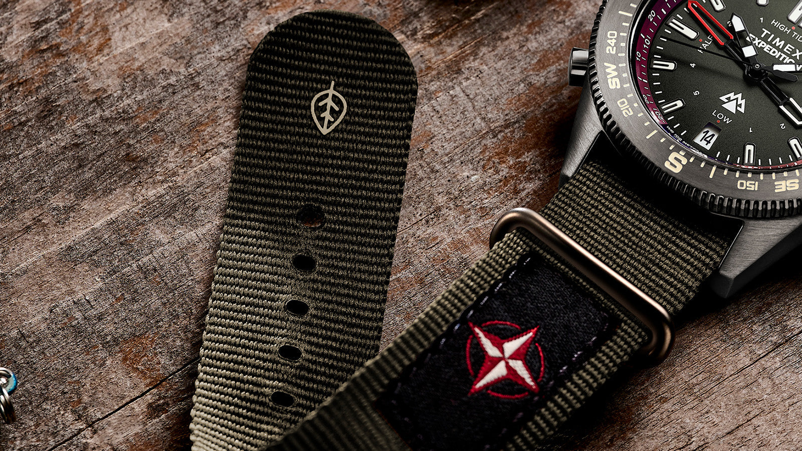 Close-up of the Expedition Tide-Temp-Compass green fabric strap, showing stitched details, buckle, and eco-friendly leaf emblem marking.
