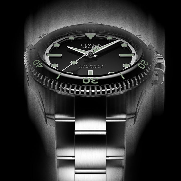 Front view of Timex Atelier automatic dive watch showing black dial, bold luminous indices, stainless steel bracelet, and engraved bezel detail.