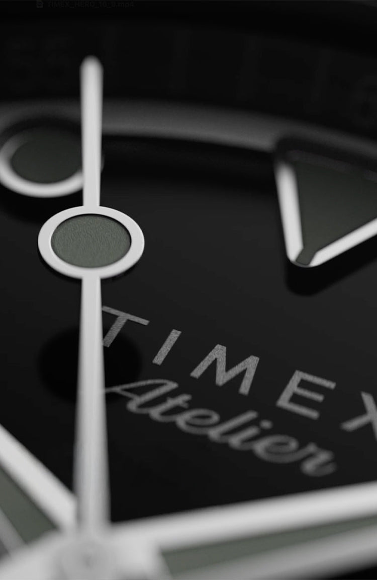 Extreme close-up of the Timex Atelier watch dial, showcasing polished silver hands and luminous markers against a glossy black background with the “Timex Atelier” logo.