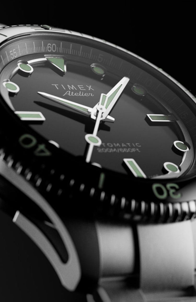 Side perspective of the Timex Atelier automatic dive watch, highlighting its stainless steel case, black rotating bezel, luminous indices, and bracelet.