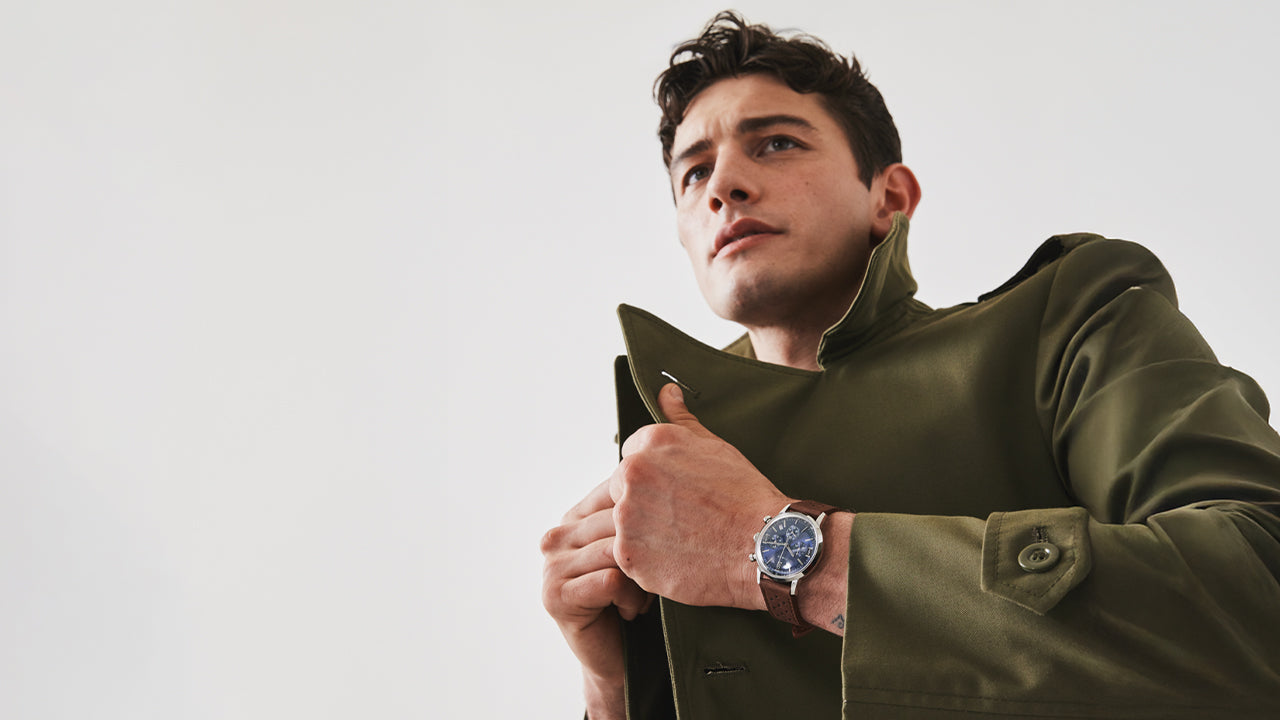 Man wearing Timex Marlin Chronograph Tachymeter with blue dial and brown leather strap while adjusting green coat collar.