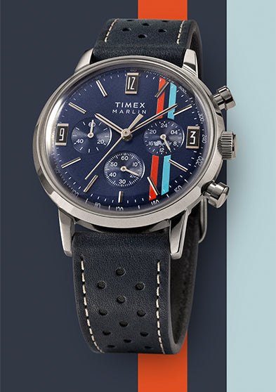 Timex Marlin Chronograph Tachymeter with blue dial, red and light blue racing stripes, and perforated leather strap displayed on a color-blocked blue and orange background.