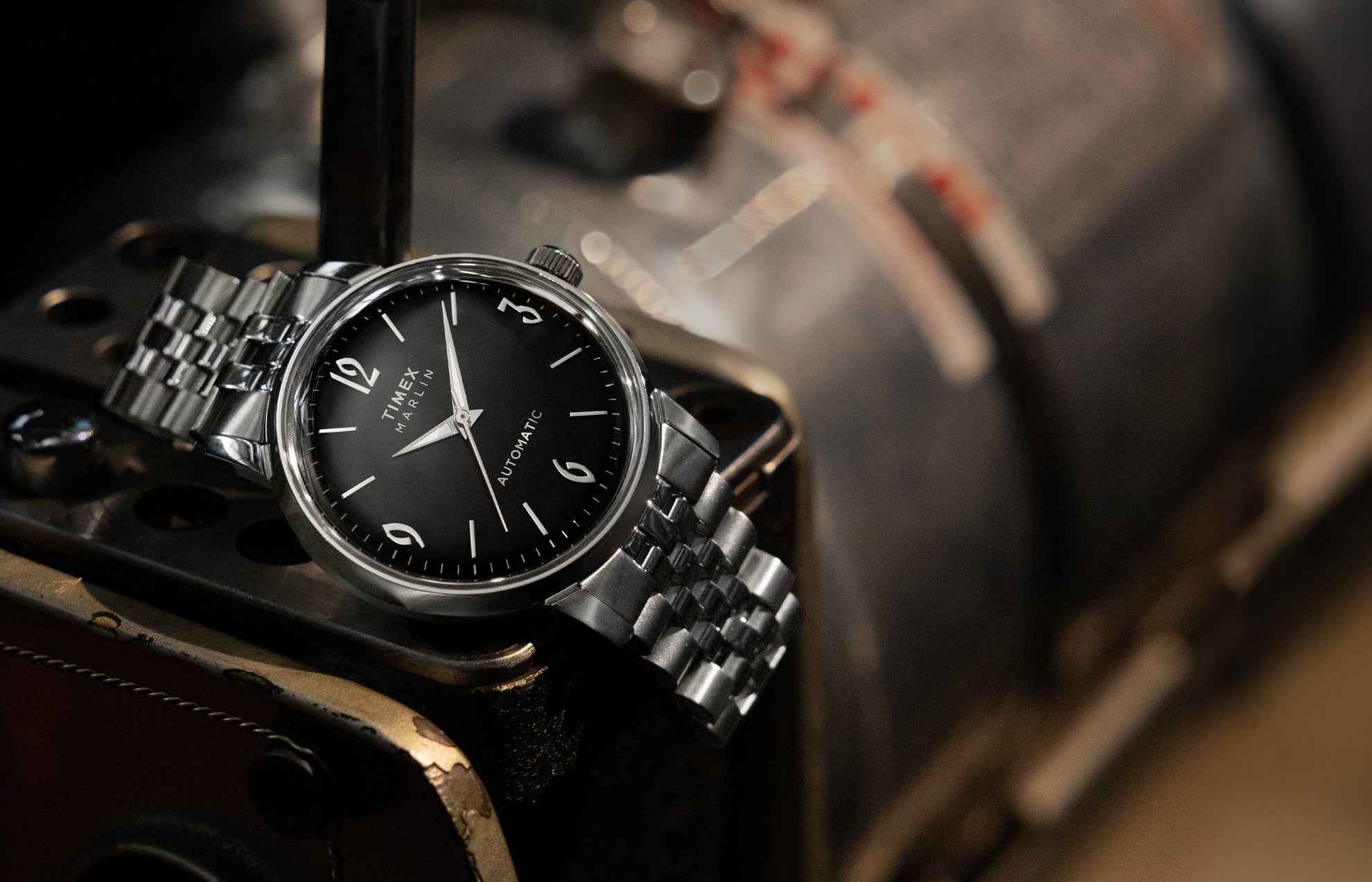 Timex Marlin Automatic with black dial and silver stainless-steel bracelet resting on a vintage metal surface.