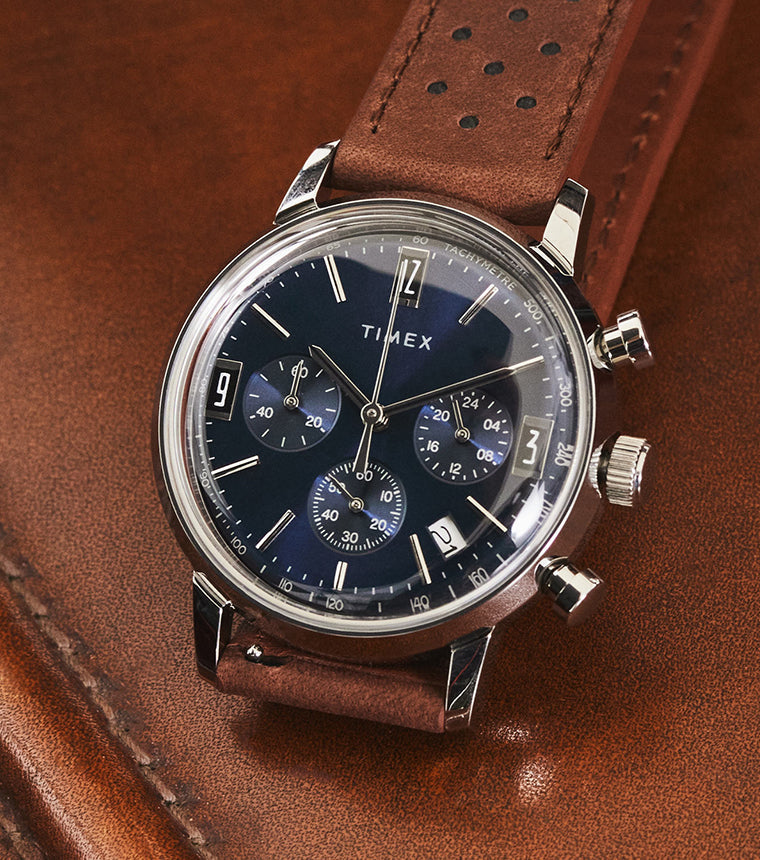 Timex Marlin Chronograph Tachymeter watch with blue dial and brown perforated leather strap resting on brown leather surface.