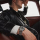 Man wearing Timex Marlin Chronograph Tachymeter with stainless-steel bracelet while relaxing in a classic car wearing a black leather jacket.