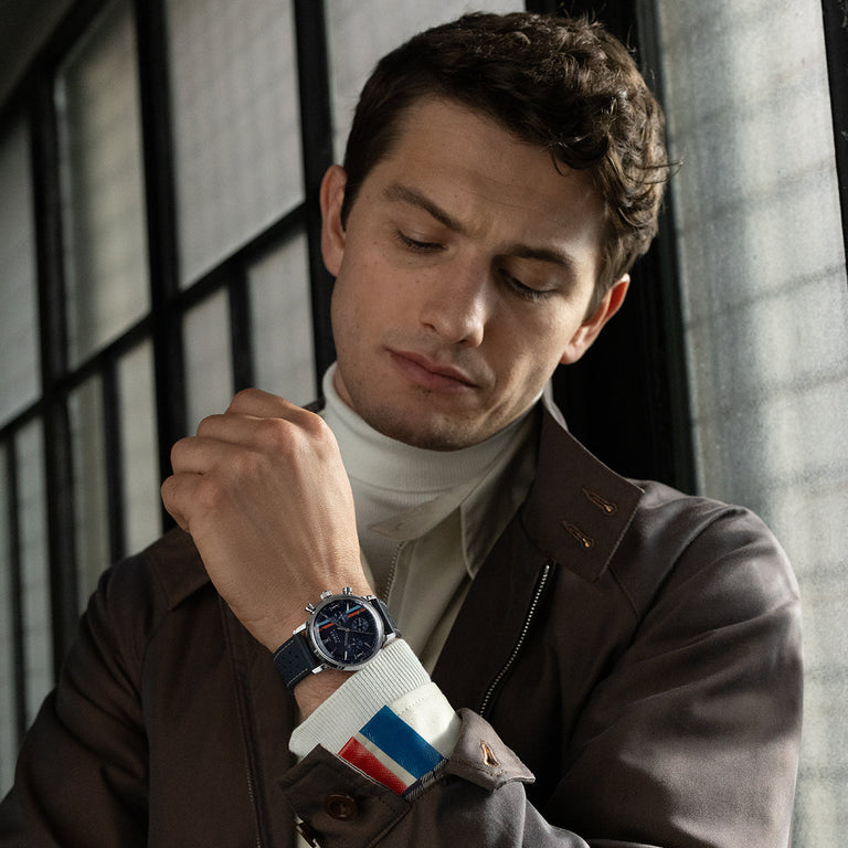 Model wearing Timex Marlin Chronograph Tachymeter with navy dial and blue strap, adjusting cuff inside an industrial-style room.