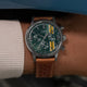 Close-up of model wearing Timex Marlin Chronograph Tachymeter with green dial, yellow accents, and brown strap beside a vintage blue race car.