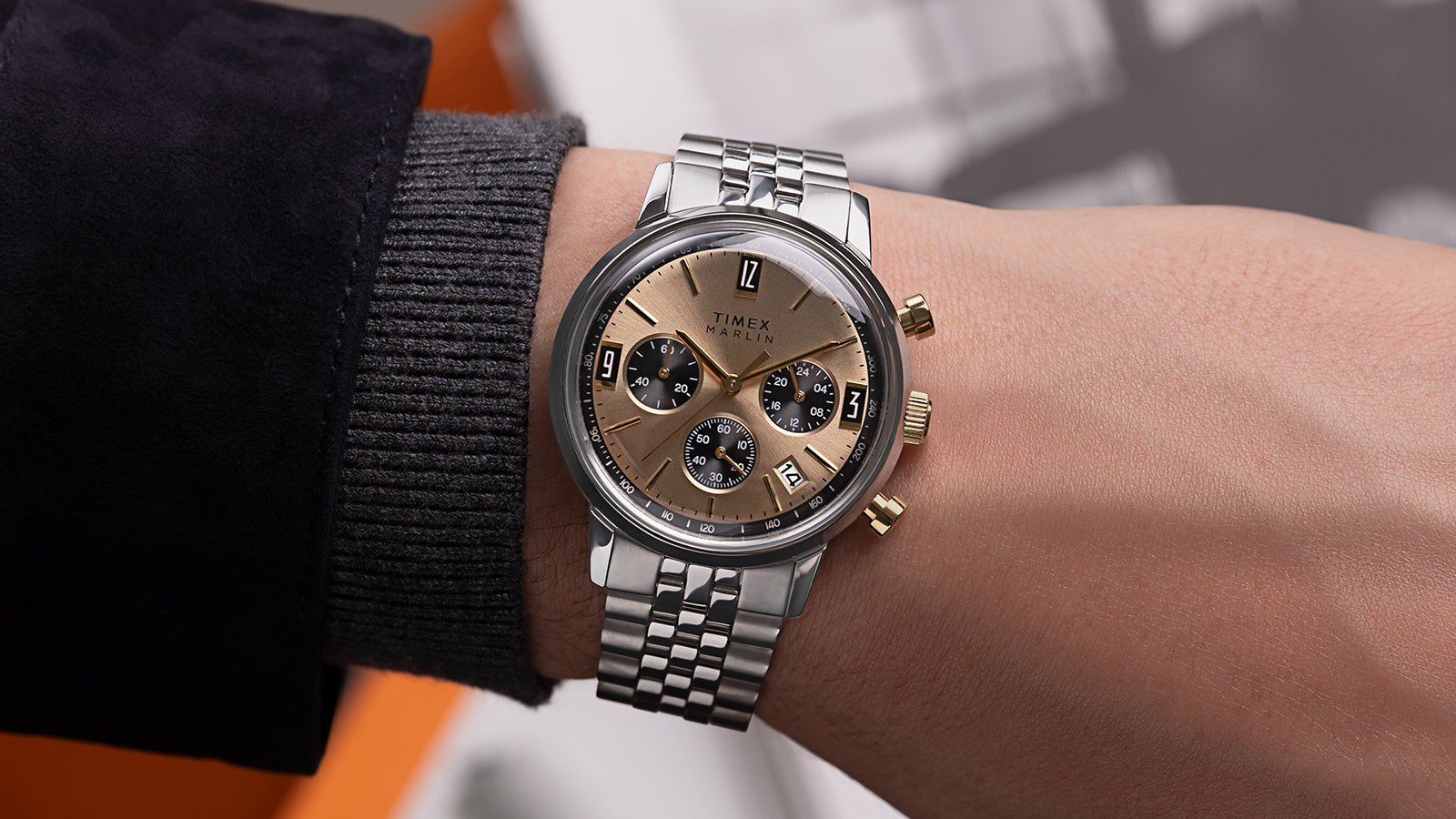 Timex Marlin Chronograph Tachymeter with champagne dial and gold accents worn on wrist, paired with a dark jacket.