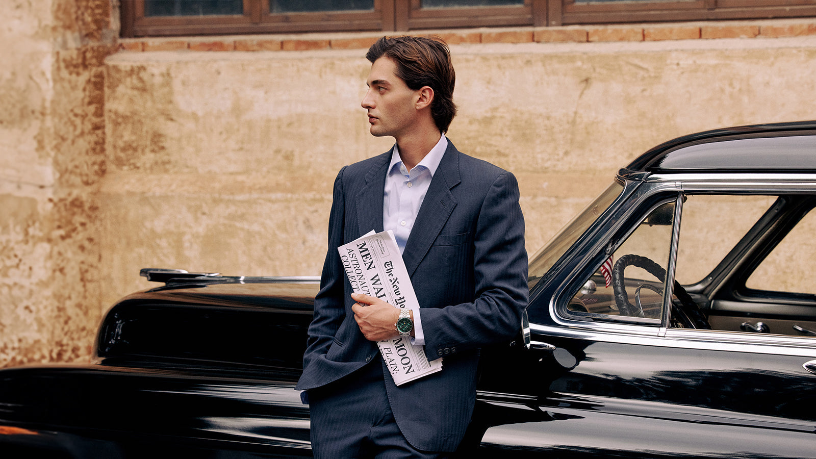 Man in a navy suit wearing the Timex Marlin Moon Phase Multifunction while holding a newspaper next to a vintage black car.