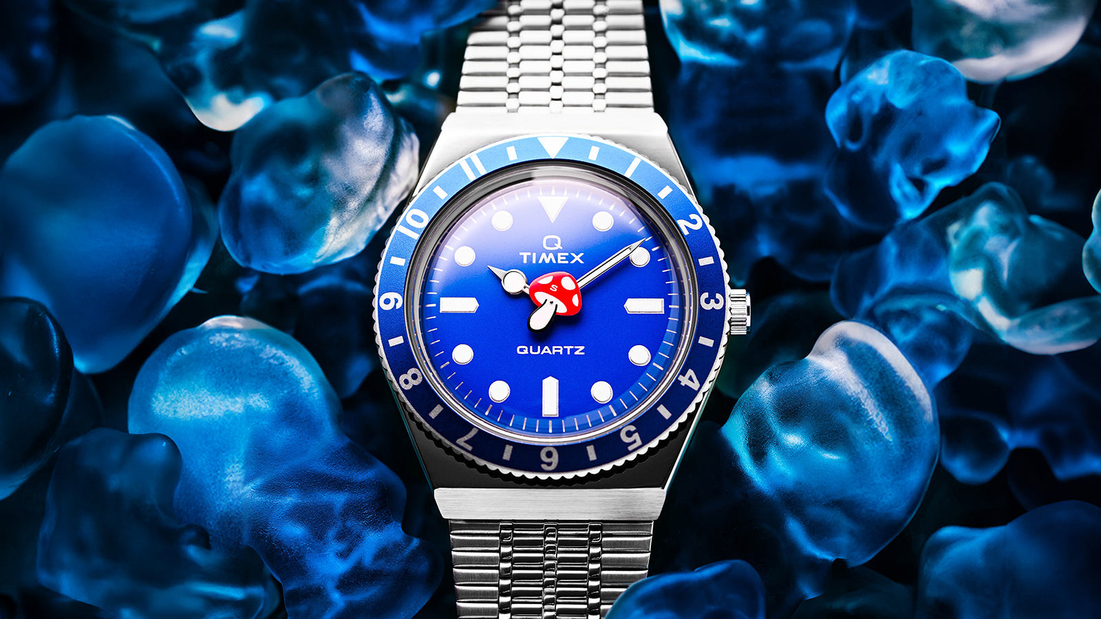 Another close-up of the Q Timex blue watch with red mushroom seconds hand surrounded by glowing blue gummy candies.