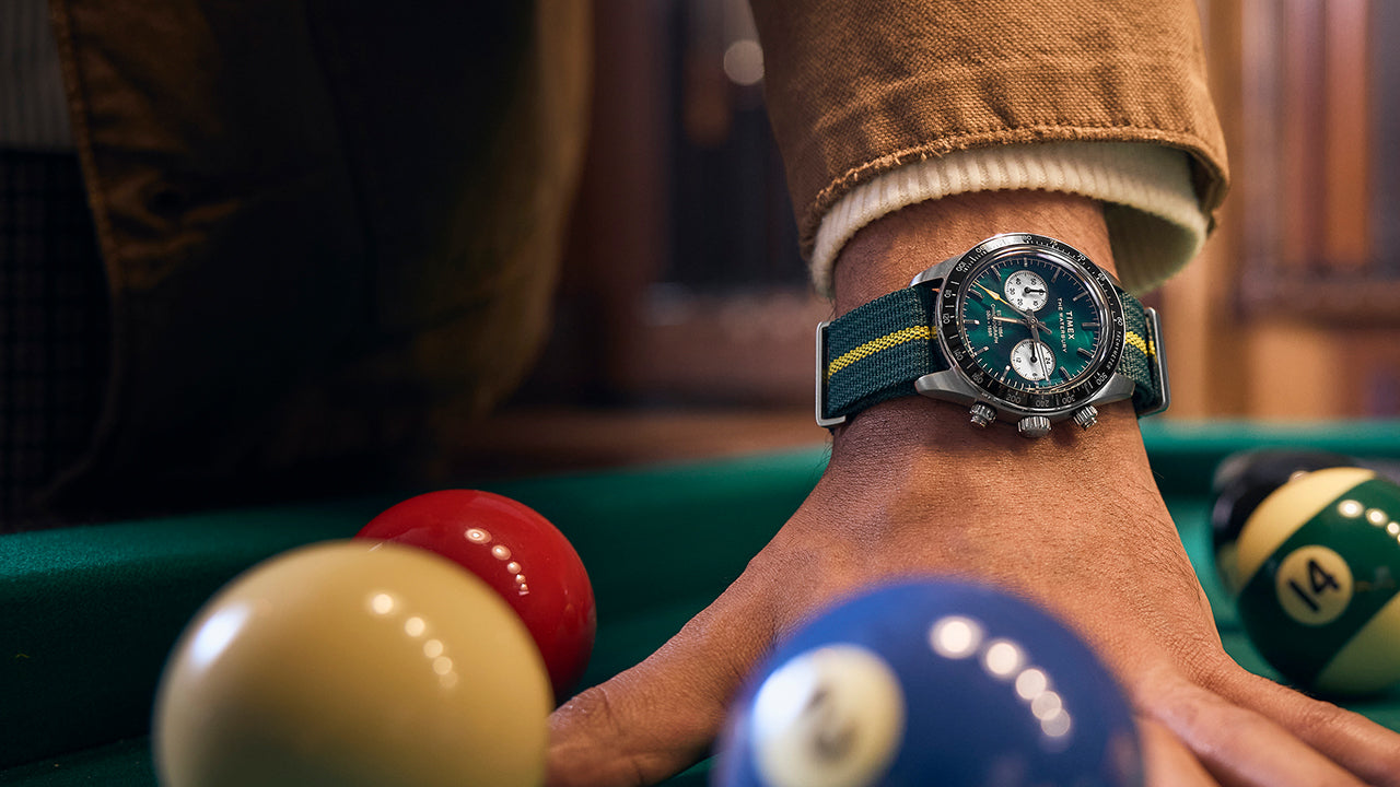 Close-up of the Timex Waterbury Heritage Chronograph with green dial and striped fabric strap worn with a tan jacket sleeve.