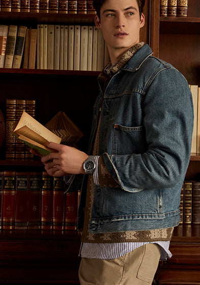 Man wearing the Timex Waterbury Metropolitan Chronograph while reading in a library, styled in denim jacket and casual layers.