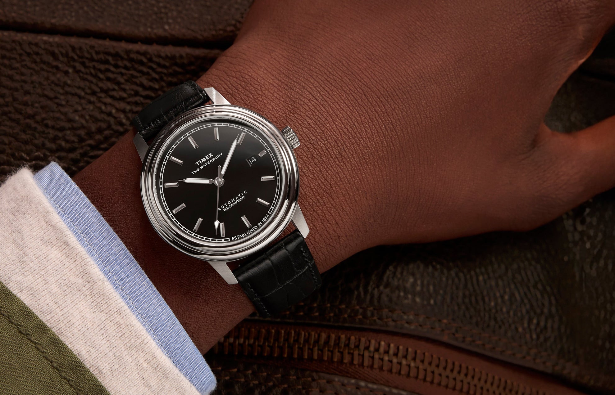 Timex Waterbury Metropolitan Automatic watch on wrist, paired with a dress shirt and jacket, showcasing the sleek black dial and classic leather strap.