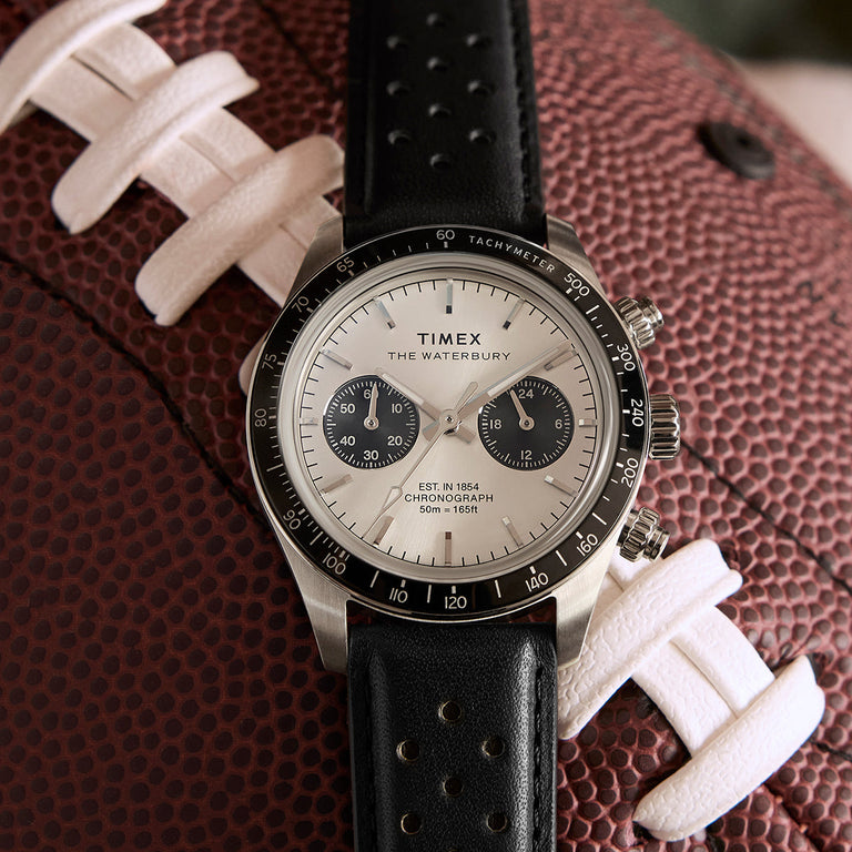 Timex Waterbury Heritage Chronograph placed on a textured football, highlighting its sporty black bezel, dual sub-dials, and perforated leather strap.