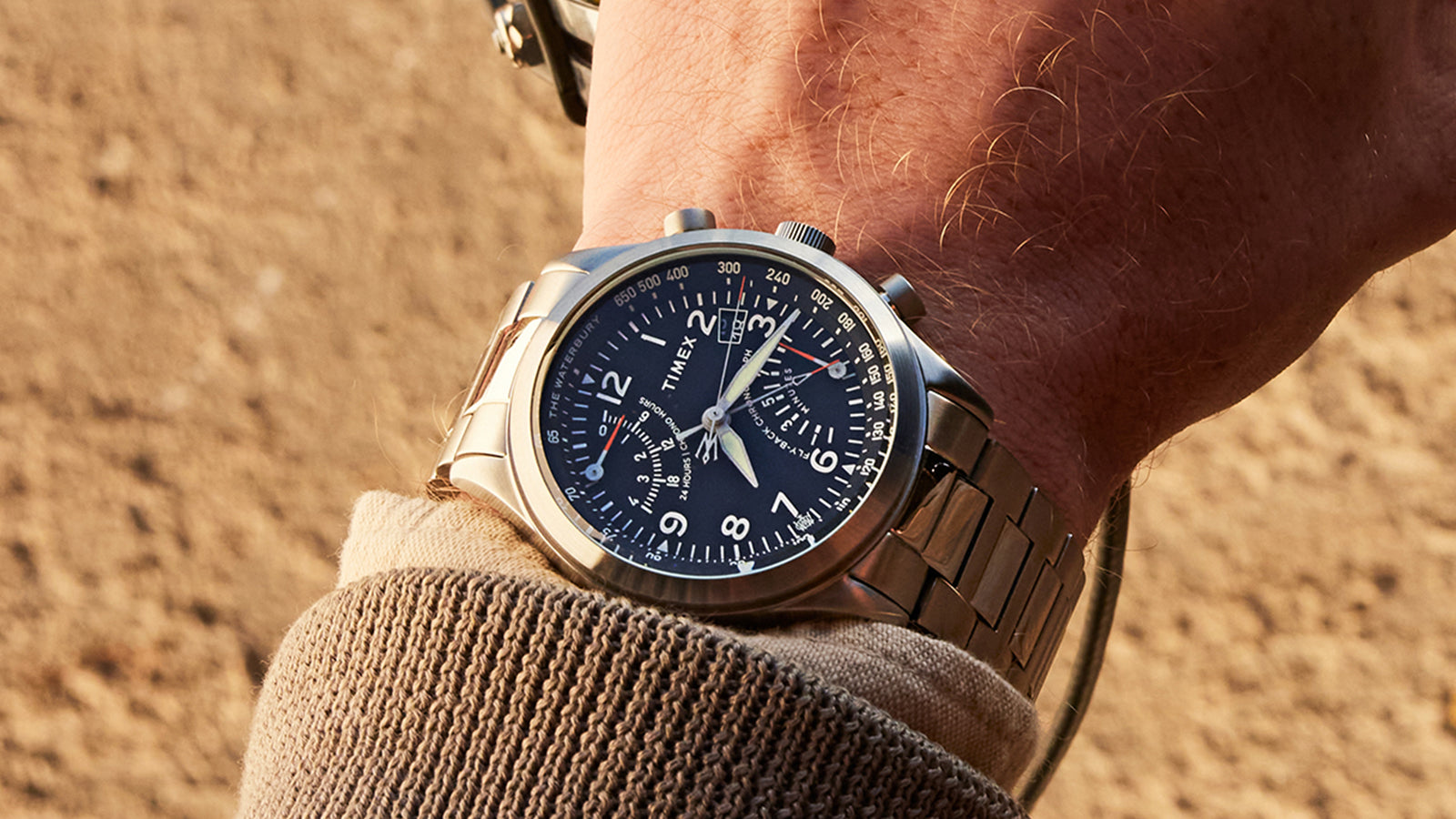 Close-up of the Timex Waterbury Traditional Fly-Back Chronograph on wrist, showing stainless steel bracelet and luminous dial under golden sunlight.