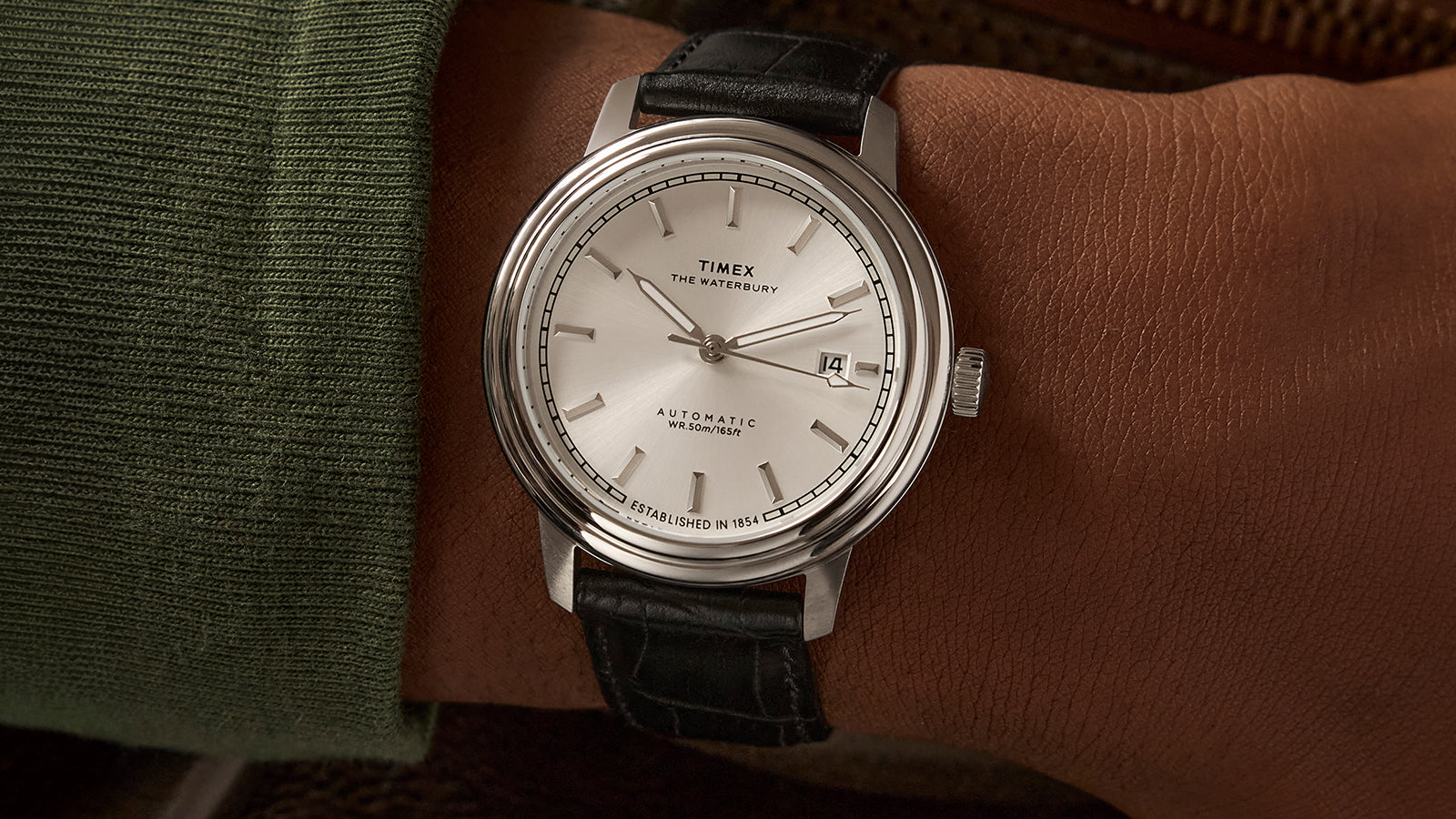 Timex Waterbury Metropolitan Automatic watch on wrist, featuring a minimalist silver dial, stainless steel case, and black leather strap with croc texture.