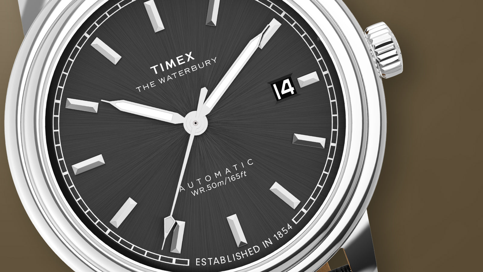 Macro view of the Timex Waterbury Metropolitan Automatic’s brushed black dial with polished indices and textured crown detailing.