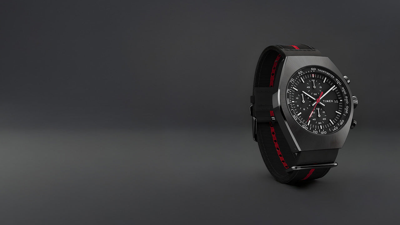 Timex Legacy Tonneau Chronograph with black dial, red accents, and black fabric strap with red stripe displayed against a dark gray background.