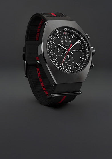 Timex Legacy Tonneau Chronograph with black dial, red accents, and black fabric strap with red stripe displayed against a dark gray background.