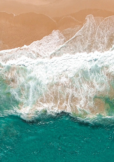 Aerial view of waves washing onto a sandy beach, symbolizing the coastal inspiration of the TIMEX® Harborside Coast collection.