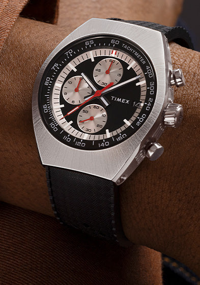 TIMEX® Legacy Tonneau Chronograph worn with a brown jacket, showing its bold tonneau-shaped case and sporty chronograph subdials.