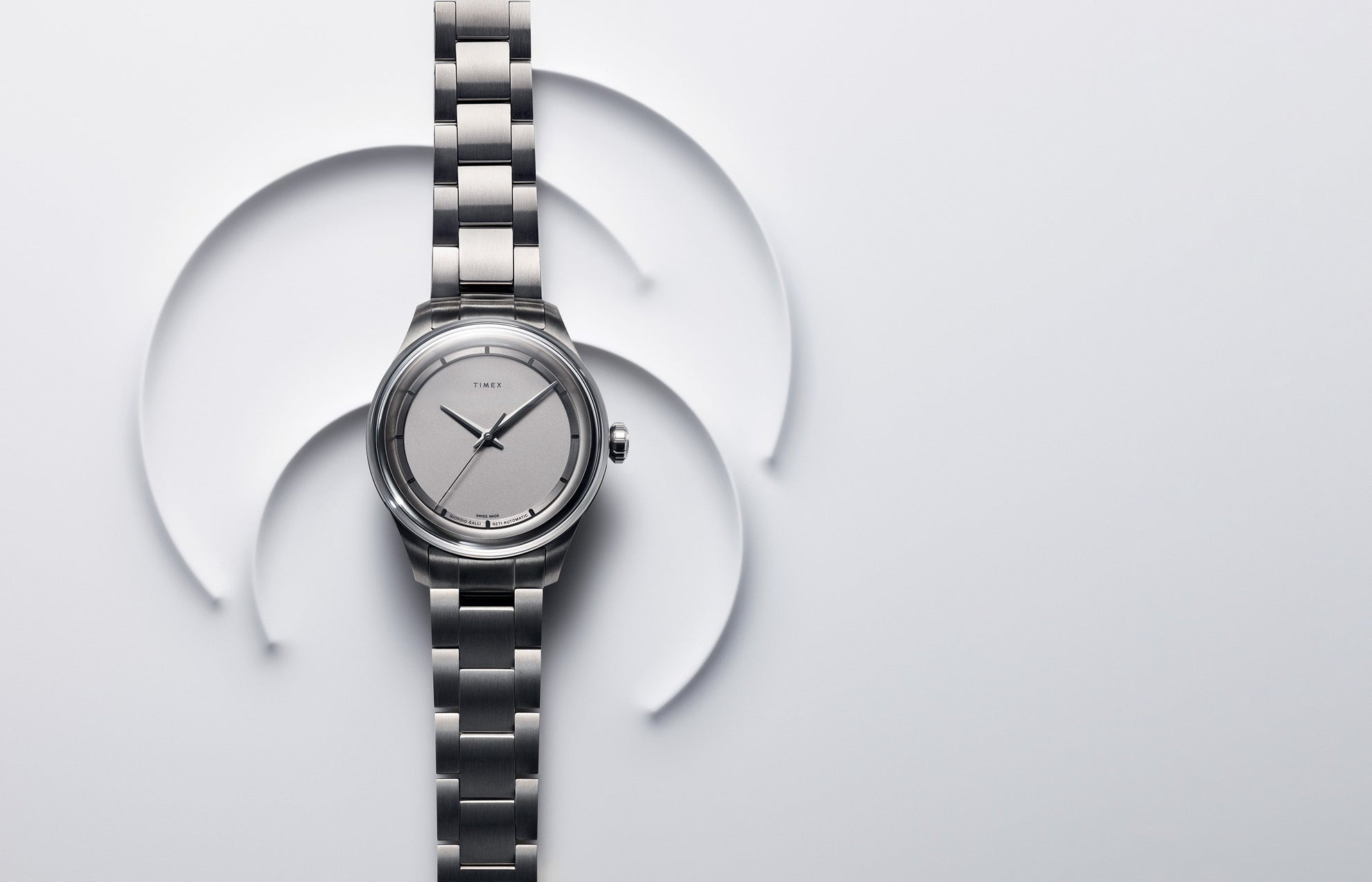 Timex Giorgio Galli S2Ti Swiss Made Automatic watch with a titanium case and silver dial, displayed on a minimalist white background with abstract circular shapes.