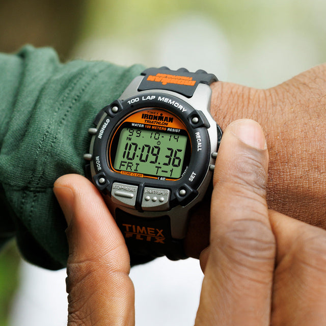 Person wearing the TIMEX® IRONMAN® Flix 100 sports watch on their wrist, pressing a button while checking the time during a workout.