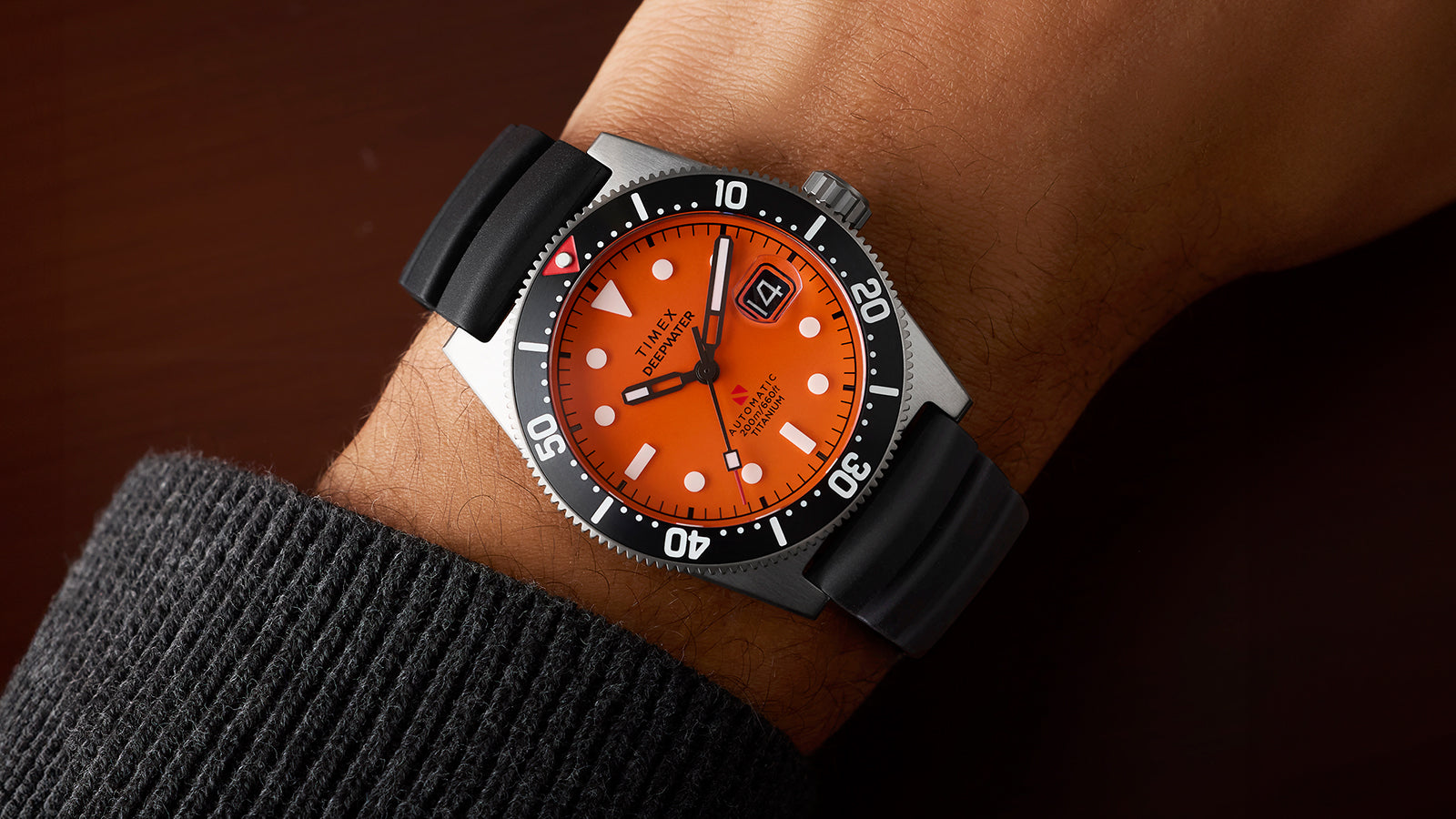 Timex Deepwater Reef 200 with an orange dial and black rubber strap worn on the wrist, showing the dive bezel and rugged titanium case in detail.